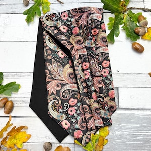 May include: A black necktie with a paisley pattern in shades of pink, cream, and teal. The tie is folded over a solid black fabric, creating a contrast in textures and colours. The paisley design features floral and swirling elements.