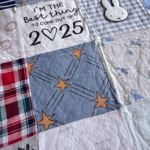 May include: A patchwork baby quilt featuring various fabric squares including a white panel with the black text I'M THE BEST THING TO COME OUT OF 2♡25, a blue square with yellow stars, a blue gingham square with a white bunny applique, and plaid.