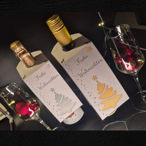 Puede incluir: Dos botellas de vino con etiquetas decorativas que dicen "Frohe Weihnachten" y un diseño de árbol de Navidad. Dos copas de vino llenas de adornos rojos y luces de hadas, creando una escena festiva.
