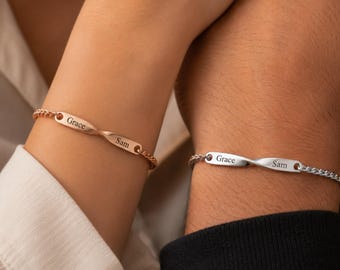 May include: Two bracelets featuring a central twisted metal bar with the engraved names Grace and Sam. One bracelet is rose gold-toned with a matching chain, while the other is silver-toned with a matching chain, both secured by thin metal links.