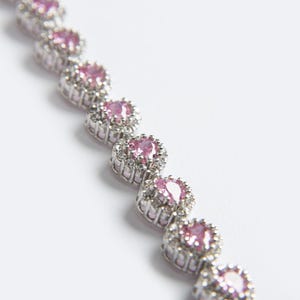 May include: A silver-toned bracelet featuring a series of pink gemstone clusters. Each cluster has a central pink stone surrounded by smaller, clear stones. The bracelet is set against a white background.