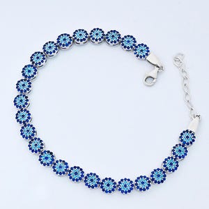 May include: Silver bracelet with a series of blue and light blue circular charms. Each charm has a floral design with a central dark blue dot. The bracelet has a clasp closure and an adjustable chain.