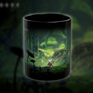Puede incluir: Taza de cerámica negra con una ilustración detallada de un personaje con vestido rojo y máscara blanca en un bosque verde. El diseño incluye una gran estructura ornamentada y setas estilizadas.