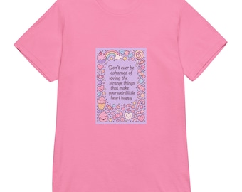 May include: A pink t-shirt featuring a rectangular graphic with the text "Don't ever be ashamed of loving the strange things that make your weird little heart happy." The graphic includes a rainbow, cupcakes, and hearts.