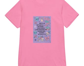 May include: Pink t-shirt with a graphic on the front. The graphic is a purple rectangle with skulls, flowers, and the text "SHE'S A 10 BUT SHE'S A TATTOOED BOOK GHOUL & SHE SCREAMS FOR MASKED MEN, SO SHE'S ACTUALLY A 13."