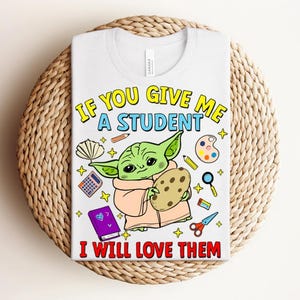 May include: White t-shirt with a cartoon character holding a cookie, surrounded by school supplies. The text reads, "IF YOU GIVE ME A STUDENT I WILL LOVE THEM" in yellow, blue, and red.