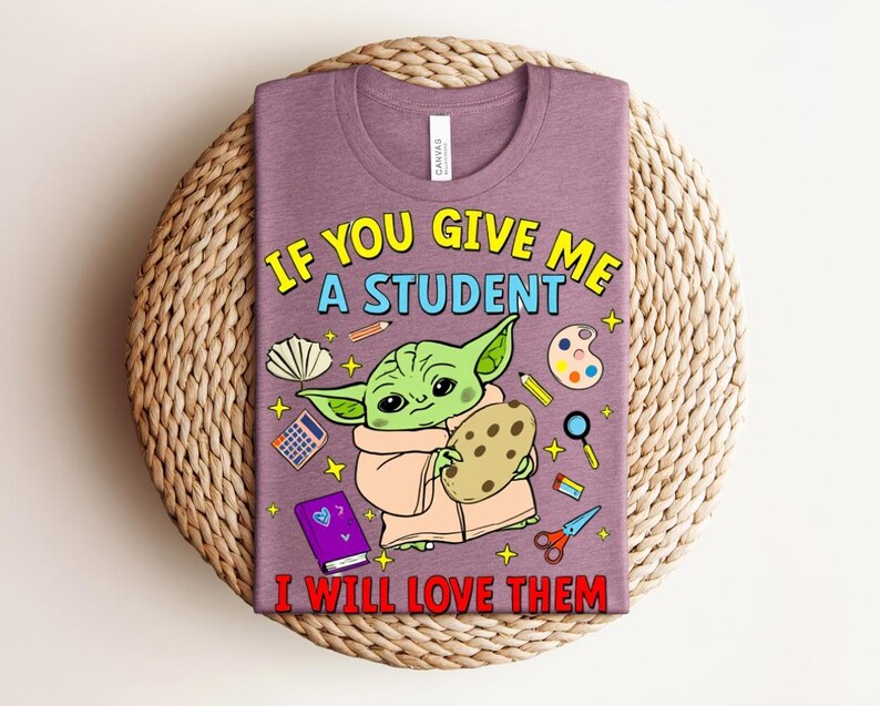 May include: A purple t-shirt with a cartoon image of a green alien-like character holding a cookie, with school supplies. The text says, "IF YOU GIVE ME A STUDENT I WILL LOVE THEM."