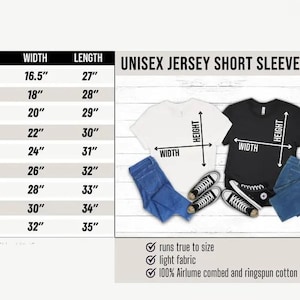 Op de afbeelding: Een wit en zwart Unisex Jersey Short Sleeve Tee met afmetingen en maattabel. De tabel toont maten XS tot 5XL met bijbehorende breedte- en lengtematen in cm. De afbeelding bevat ook een blauwe jeans en sneakers.