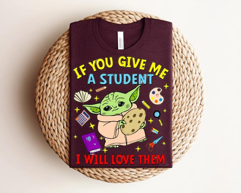 May include: Burgundy t-shirt featuring a green alien-like character holding a cookie, with school supplies graphics. The text reads "IF YOU GIVE ME A STUDENT I WILL LOVE THEM" in yellow and red.