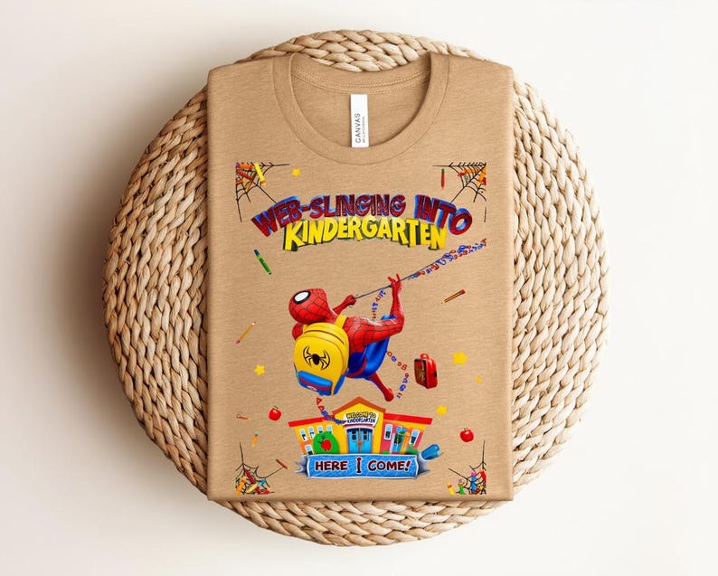 Pu&ograve; includere: T-shirt color cachi con grafica colorata di Spider-Man che si dondola, con la scritta "Web-Slinging Into Kindergarten". Il design include una scuola e la frase "Here I Come!" in un carattere giocoso.
