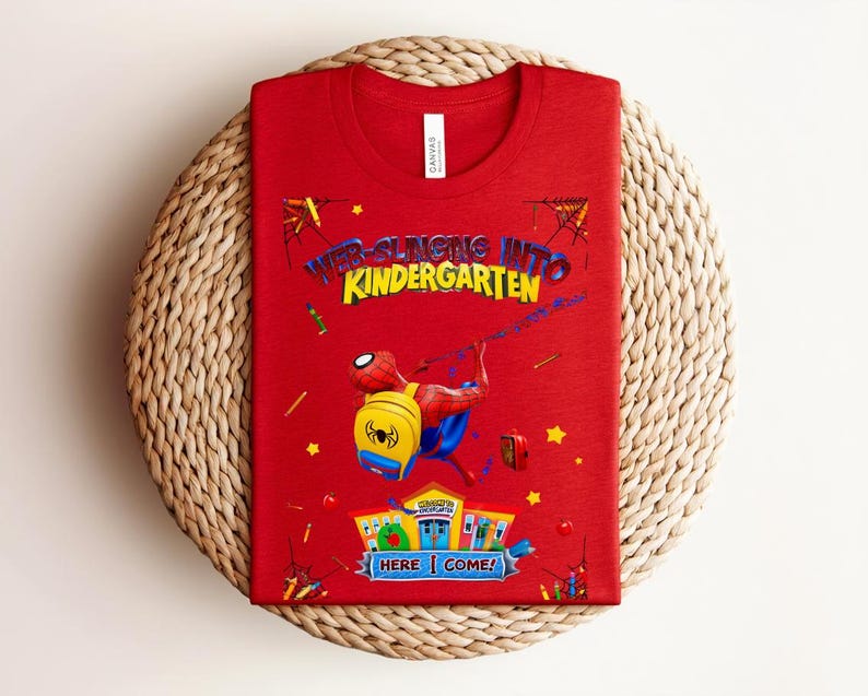 Pu&ograve; includere: Una maglietta rossa con una grafica di Spider-Man e la scritta "Web-Slinging Into Kindergarten". Il design include un Spider-Man dei cartoni animati, uno zaino giallo e la frase "Here I Come!" in un banner colorato.