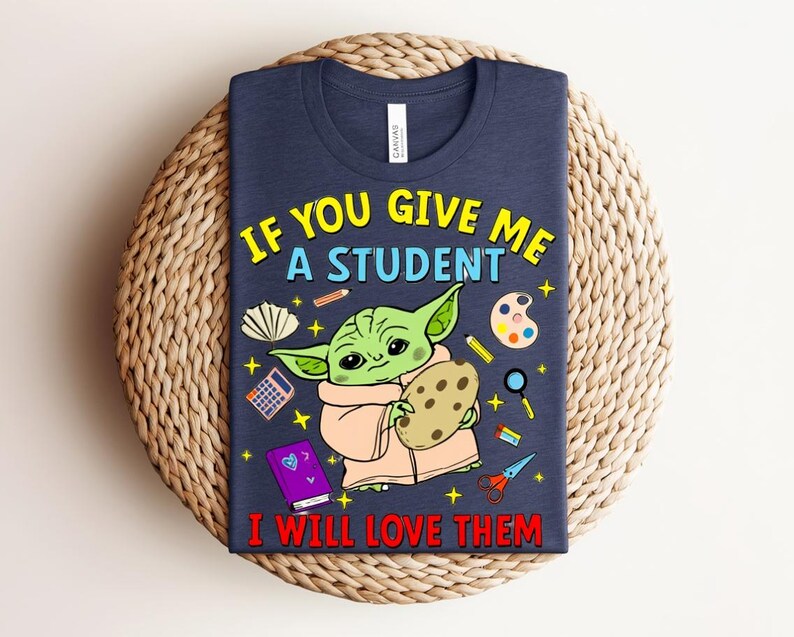 May include: A navy blue t-shirt with a cartoon character holding a cookie, surrounded by school-themed illustrations. The text reads "IF YOU GIVE ME A STUDENT I WILL LOVE THEM" in yellow and red.
