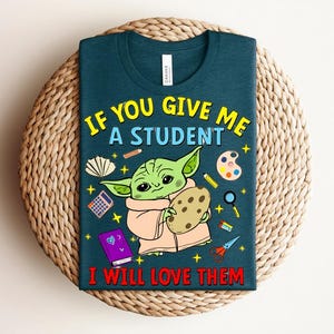 May include: Teal t-shirt with a cartoon character holding a cookie, surrounded by school-themed graphics. The text reads, "IF YOU GIVE ME A STUDENT I WILL LOVE THEM." The design includes a calculator, paint palette, and scissors.