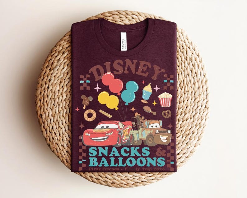 May include: A maroon t-shirt with a graphic featuring the word "Disney" in a retro font, balloons, and cartoon cars. The shirt also has the words "Snacks & Balloons" and "Pixar Friends" printed on it.