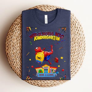 Pu&ograve; includere: T-shirt blu navy con Spider-Man, zaino, la scritta "WEB-SLINGING INTO KINDERGARTEN" e "HERE I COME!". Il design include stelle, matite e un edificio scolastico.