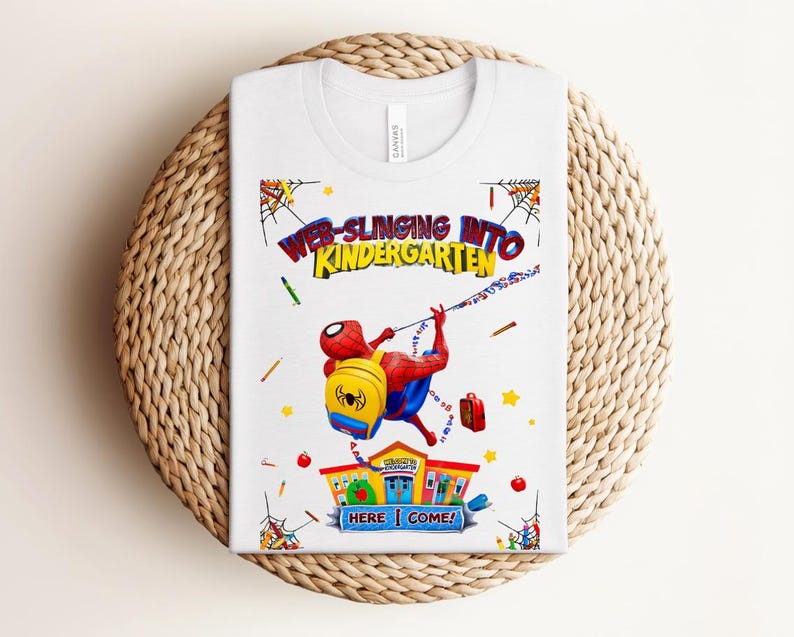 Pu&ograve; includere: T-shirt bianca con una grafica colorata di Spider-Man che si lancia verso la scuola materna. Il design include il testo "WEB-SLINGING INTO KINDERGARTEN" e "HERE I COME!" con illustrazioni a tema scolastico.