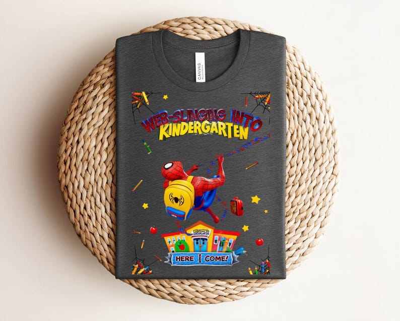 Pu&ograve; includere: T-shirt grigio scuro con una grafica colorata di Spider-Man e la scritta "WEB-SLINGING INTO KINDERGARTEN". Il design include un edificio scolastico, stelle e materiale scolastico. Un design divertente per bambini.