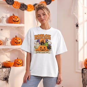 May include: A white short-sleeved t-shirt featuring a colorful graphic print with the text ROBLOX PUMPKIN SEASON and HARVEST BLOCK PARTY. The design includes a large orange jack-o'-lantern, a mummy, a green monster, a ghost, and a dark castle.