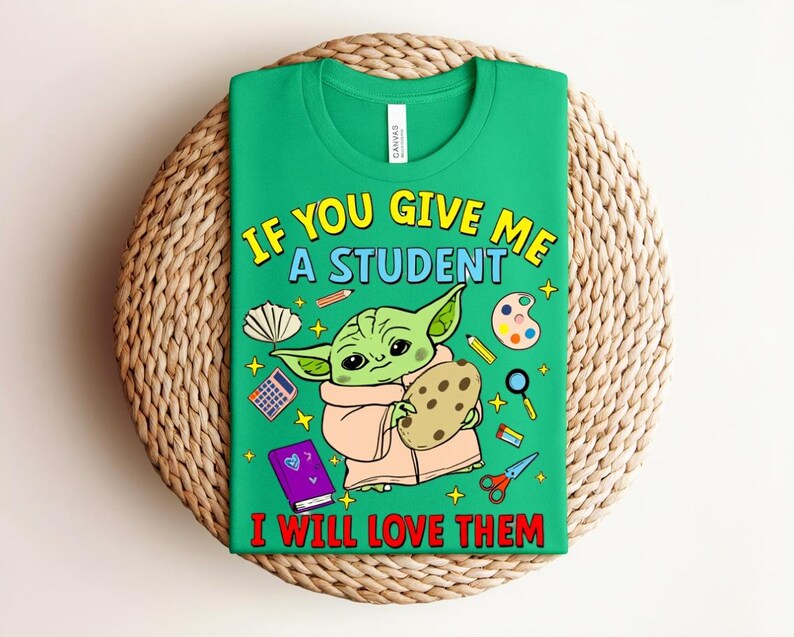May include: Green t-shirt featuring the text "IF YOU GIVE ME A STUDENT I WILL LOVE THEM" and a cartoon character holding a cookie. The shirt includes school-related graphics such as a calculator and paint palette.
