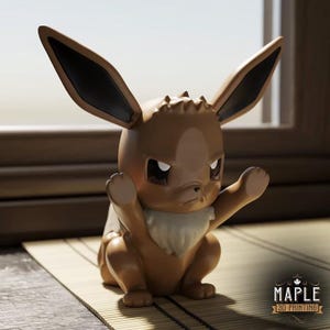 Op de afbeelding: Een bruin Eevee-beeldje met grote oren en een strenge uitdrukking. De figuur heeft een witte bontkraag en poseert met opgeheven armen. Het Maple 3D Printing-logo is rechtsonder zichtbaar. Het beeldje staat op een bamboemat.