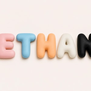 May include: The name ETHAN spelled out in individual, rounded, three-dimensional letters. The letter E is light pink, T is light blue, H is light orange, A is off-white, and N is black. Each letter has a smooth, matte, bubble-like appearance.