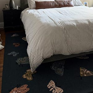 May include: A bedroom scene featuring a bed with a striped comforter and a brown leather bolster pillow. Above the bed, six framed black and white photos are displayed. A dark rug with butterfly designs is on the floor.
