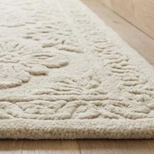 Puede incluir: Alfombra rectangular color crema con un estampado floral. La alfombra est&aacute; hecha de un material suave y texturizado y se coloca sobre un piso de madera junto a un rodapi&eacute; de madera. El dise&ntilde;o de la alfombra presenta motivos florales en relieve.