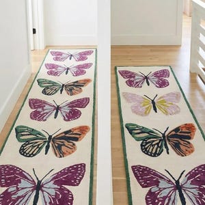 May include: Two rectangular rugs featuring butterfly patterns. The rugs have a cream backdrop with a green border. The butterflies are in shades of purple, orange, green, and yellow. The rugs are positioned in a hallway.