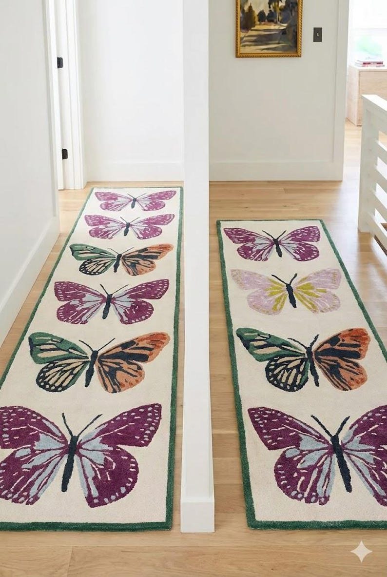 May include: Two rectangular rugs featuring butterfly patterns. The rugs have a cream backdrop with a green border. The butterflies are in shades of purple, orange, green, and yellow. The rugs are positioned in a hallway.