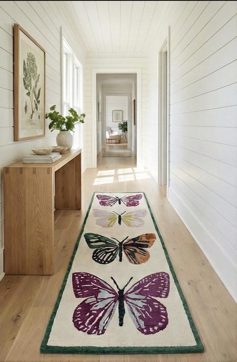 May include: A hallway runner rug with four butterfly designs in shades of purple, green, and brown on an off-white background. The rug has a green border and is placed on a light wood floor.