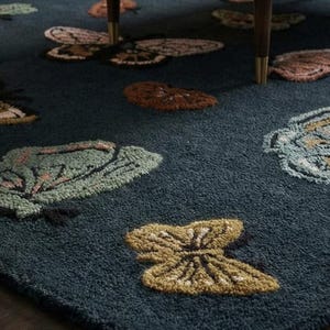 May include: A dark teal rug with a repeating butterfly pattern in shades of brown, green, and yellow. The butterflies are scattered across the rug's surface, creating a whimsical and nature-inspired design. The rug is made of a soft, textured material.