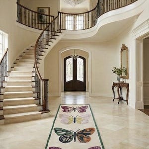 May include: A luxurious entrance hall with a sweeping staircase and a rug adorned with butterfly motifs. The rug displays four vibrant butterfly designs on a cream backdrop, edged with green. A large crystal chandelier illuminates the space.