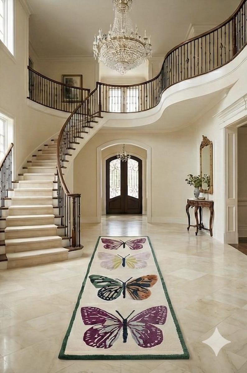 May include: A luxurious entrance hall with a sweeping staircase and a rug adorned with butterfly motifs. The rug displays four vibrant butterfly designs on a cream backdrop, edged with green. A large crystal chandelier illuminates the space.