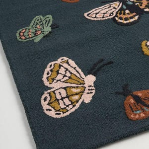 May include: A dark teal rug featuring a repeating pattern of colorful butterflies. The butterflies have detailed wing patterns in shades of pink, brown, green, and yellow. The rug has a textured, plush appearance.