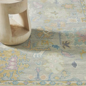 Peut inclure: Un tapis bleu clair avec un motif floral dans les tons de jaune, rose et bleu. Une petite table d'appoint en bois clair avec une bougie est posée sur le tapis. Le tapis a un aspect vieilli.