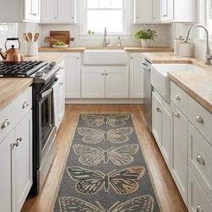May include: A kitchen with white cabinets, wooden worktops, and a grey runner rug featuring large butterfly designs. The rug is centered on the wooden floor, adding a decorative element to the space. The kitchen has a farmhouse sink and stainless steel appliances.