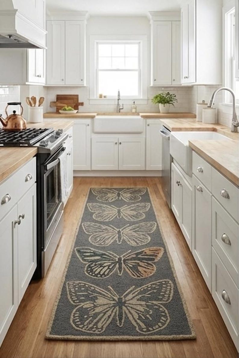 May include: A kitchen with white cabinets, wooden worktops, and a grey runner rug featuring large butterfly designs. The rug is centered on the wooden floor, adding a decorative element to the space. The kitchen has a farmhouse sink and stainless steel appliances.
