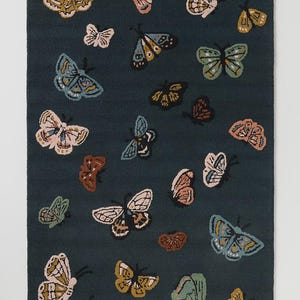 May include: A rectangular rug with a dark teal background features a pattern of various colorful butterflies. The butterflies are in shades of pink, yellow, blue, and brown, with detailed wing patterns. The rug is a decorative home accent.
