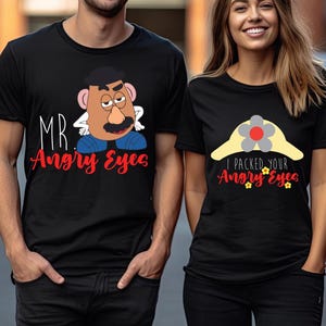 May include: Two black t-shirts with cartoon designs. One has a Mr. Potato Head graphic and the text "Mr. Angry Eyes" in red. The other features a hat design with the text "I Packed Your Angry Eyes".
