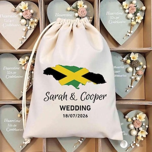 May include: A white drawstring bag with a Jamaican flag design, the names "Sarah & Cooper", the word "WEDDING", and the date "18/07/2026" printed on it. The bag is surrounded by heart-shaped decorations.