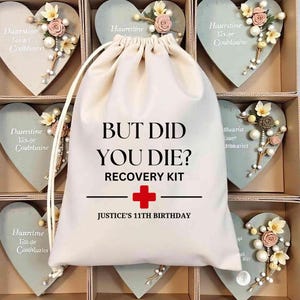 May include: A white drawstring bag with the text "BUT DID YOU DIE? RECOVERY KIT" and a red cross. Below the cross is "JUSTICE'S 11TH BIRTHDAY". The bag is in a box with heart-shaped decorations.