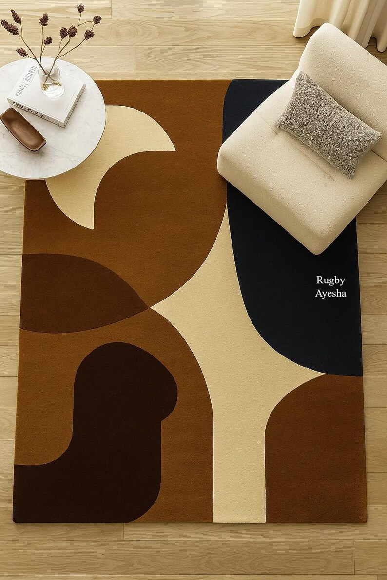 Op de afbeelding: Een rechthoekig vloerkleed met een abstract ontwerp in bruin-, beige- en marineblauwtinten. Het kleed heeft gebogen vormen en een gestructureerd oppervlak. De tekst "Rugby Ayesha" is zichtbaar op het kleed.