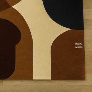 Op de afbeelding: Een modern vloerkleed met een abstract geometrisch ontwerp. Het heeft grote, gebogen vormen in bruin, beige en marineblauw. De tekst "Rugby Ayesha" is op het vloerkleed gedrukt.