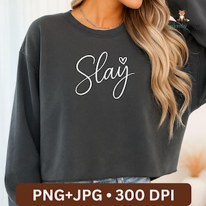 Op de afbeelding: Donkergrijze cropped sweatshirt met het woord "Slay" in witte letters, een klein hartje boven de "y". De onderkant van de afbeelding heeft de tekst "PNG+JPG • 300 DPI" in een bruine rechthoek.
