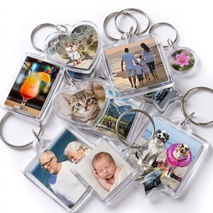 May include: A collection of clear acrylic keychains in various shapes, each featuring a different image. The keychains display photos of a family, a kitten, a cocktail, a flower, and other images. Each keychain has a silver metal ring.