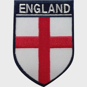 May include: Embroidered patch featuring the flag of England. The patch has a white background with a red cross, a navy blue border, and the word "ENGLAND" in white letters at the top.