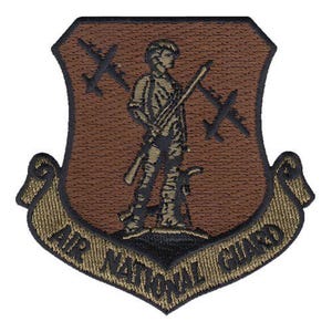 May include: Embroidered patch featuring a soldier holding a rifle, set against a brown shield with two airplanes. The words "AIR NATIONAL GUARD" are displayed on a banner below the shield. The patch has a textured appearance.