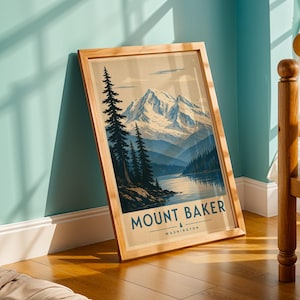May include: A framed art print featuring a stylized illustration of Mount Baker in Washington, showcasing a snow-capped mountain peak, dark evergreen trees, and a calm lake. The text MOUNT BAKER and WASHINGTON is printed in blue at the bottom.