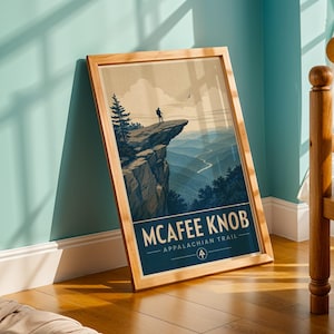 May include: A framed vertical poster featuring a stylized illustration of McAfee Knob on the Appalachian Trail. The artwork depicts a hiker standing on a rocky cliff overlooking a mountain range, with the text MCAFEE KNOB APPALACHIAN TRAIL below.