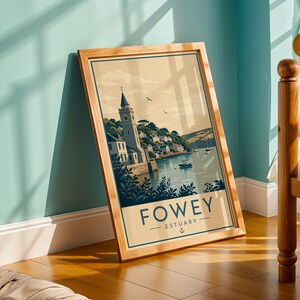 May include: A framed art print featuring a vintage-style illustration of Fowey Estuary. The artwork depicts a coastal town with a church tower, boats on the water, and the text "FOWEY - ESTUARY". The print has a light brown background and is framed in light wood.
